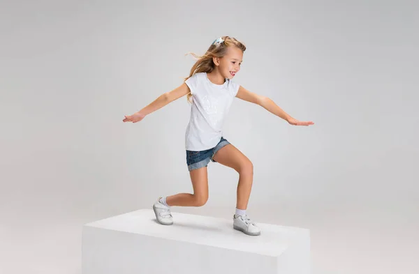 Повнометражний портрет усміхненої дівчини в повсякденному одязі, що стоїть на великій коробці ізольовано на білому фоні студії. Концепція щасливого дитинства . — стокове фото