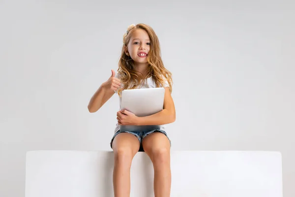 白いスタジオの背景に隔離された大きな箱の上に座ってカジュアルな服の中にかわいい女の子の肖像画。幸せな子供時代のコンセプト. — ストック写真