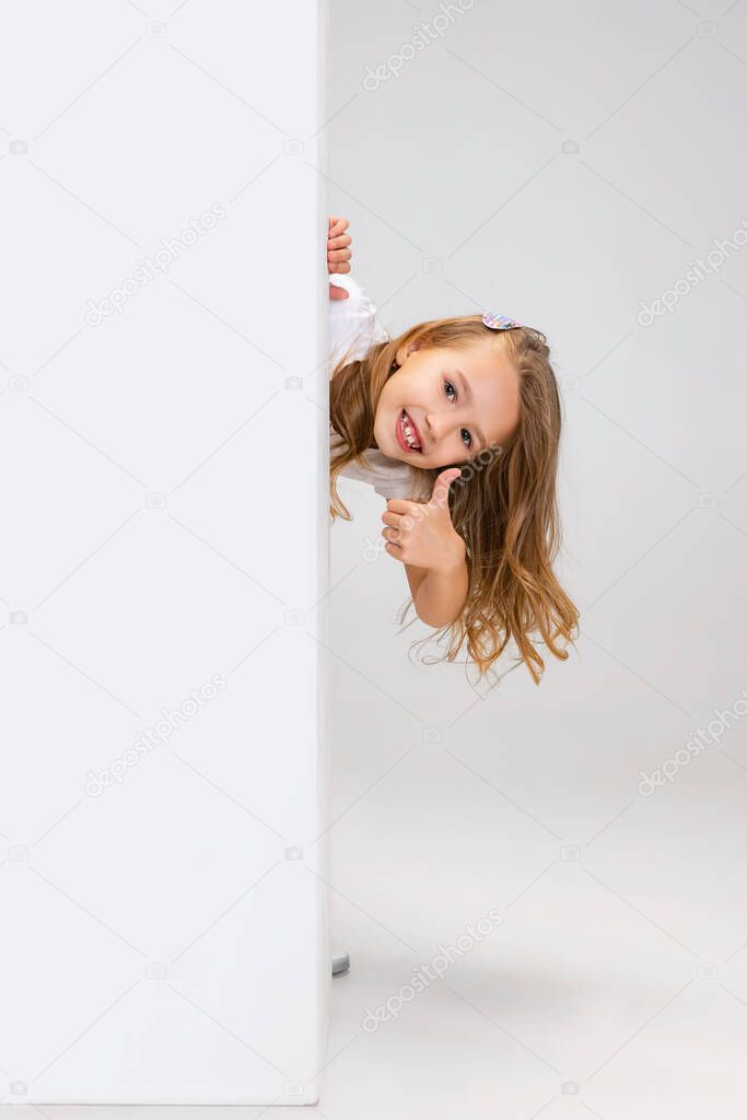 One cute beautiful little girl playing isolated on gray studio background. Human emotions, facial expression concept.