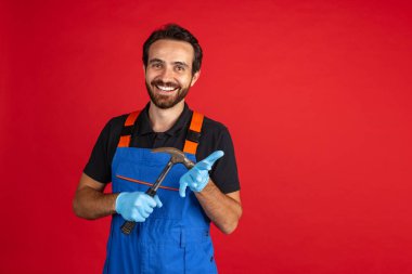 Komik sakallı genç bir adam, erkek oto tamircisi ya da kırmızı stüdyo arka planında mavi iş tulumu giyen. Yüz duyguları kavramı