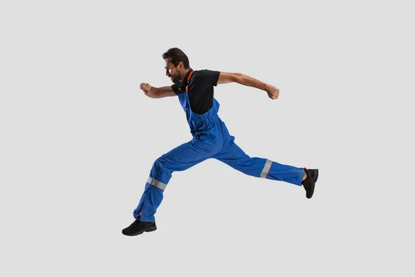 Portrait of young man, male auto mechanic in dungarees running isolated over white studio background. Concept of labor, occupation, funny meme emotions — Stock Photo, Image