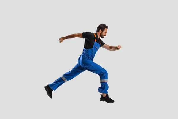 Portrait of young man, male auto mechanic in dungarees running isolated over white studio background. Concept of labor, occupation, funny meme emotions — Stock Photo, Image