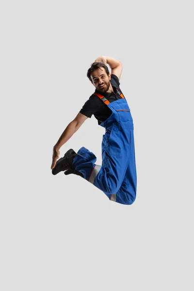 Retrato cómico de un joven, mecánico de automóviles en Dungarees saltando, volando aislado sobre fondo blanco del estudio. Concepto de ocupación, emociones divertidas meme — Foto de Stock