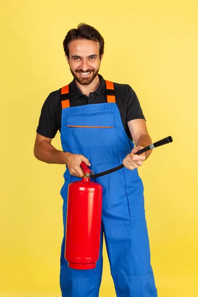 Half-length portrait of smiling young bearded man, male auto mechanic or fitter wearing blue work dungarees isolated over yellow studio background. — Stock Photo, Image