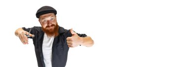 Beyaz stüdyo arka planında izole edilmiş şık bir kızıl sakallı adam, berber ya da kuaför. Kesme araçları tutuluyor.