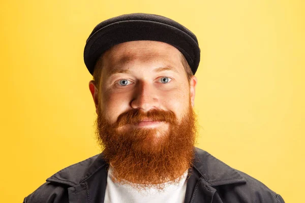 Portrait en gros plan d'un élégant homme à barbe rouge, coiffeur au chapeau noir regardant la caméra isolée sur fond jaune. Concept d'émotions, de sentiments. — Photo