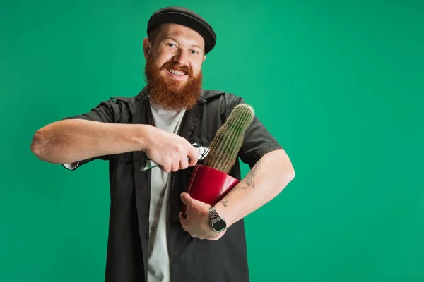 Comic portrait of stylish red-bearded man, barber in black cap having fun isolated over green background. Concept of emotions, feelings. — Stock Photo, Image