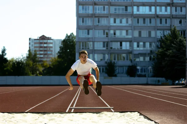 Ung kaukasisk idrottsman, manlig idrottsman, löpare hoppar högt på offentliga stadion, sport domstol eller löparbana utomhus. Sommar sport spel. — Stockfoto