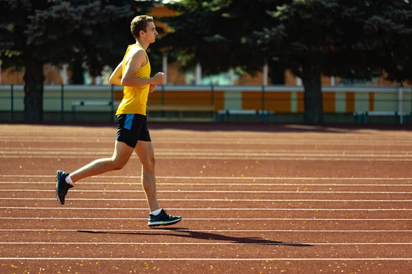 Jeune homme sportif caucasien, athlète masculin, jogging coureur au stade public, terrain de sport ou piste de course à l'extérieur. Jeux de sport d'été. — Photo