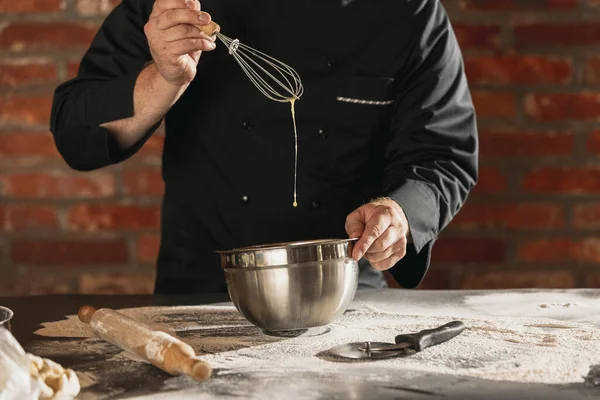 Cropped image of male chef, cook in black kitchen uniform make bread dough at cafe, restaurant kitchen. Concept of healthy diet, national cuisine.