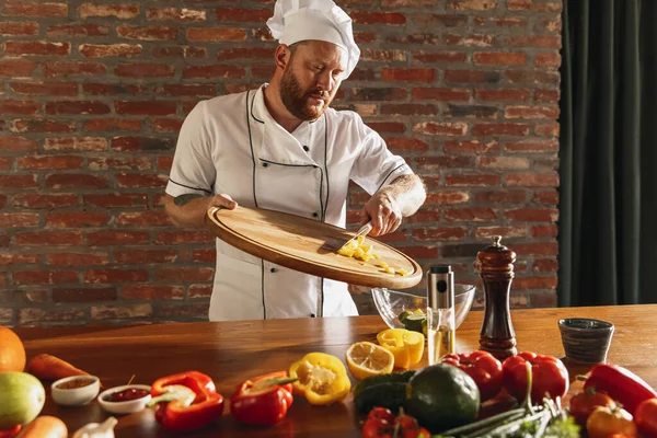 Jovem caucasiano homem de barba vermelha, chef cozinhar salada de legumes frescos no café, cozinha restaurante. Conceito de uma dieta correta e saudável. — Fotografia de Stock