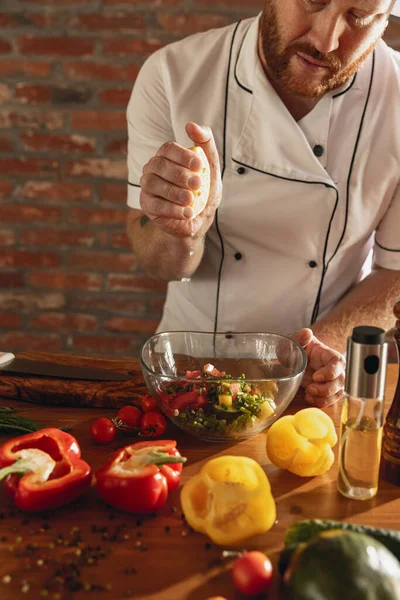 Giovane caucasico con la barba rossa, chef che cucina insalata di verdure fresche nel bar, cucina del ristorante. Concetto di una dieta corretta e sana. — Foto Stock