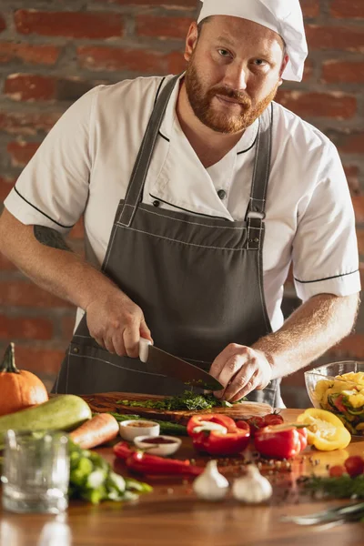 Chef profesional en uniforme preparando verduras frescas en la tabla de  cortar en la cocina del restaurante concepto culinario