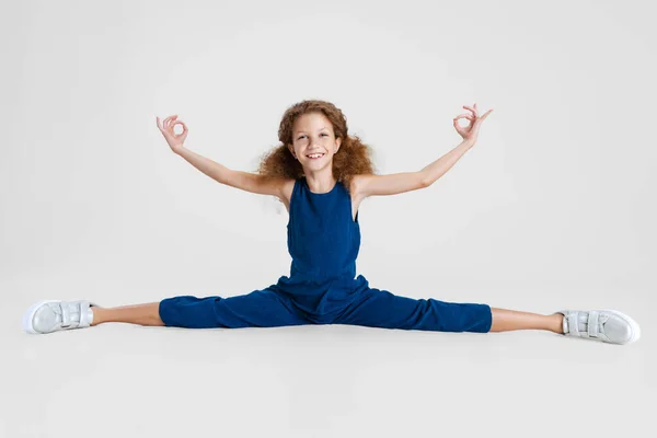 Portrait of little Caucasian cute girl in blue stylish jumpsuit sitting on a twine and having fun isolated over white studio background. — Stock Photo, Image