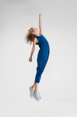 Beyaz stüdyo arka planında, mavi şık tulumlu, küçük beyaz bir kız elini uzatıyor..