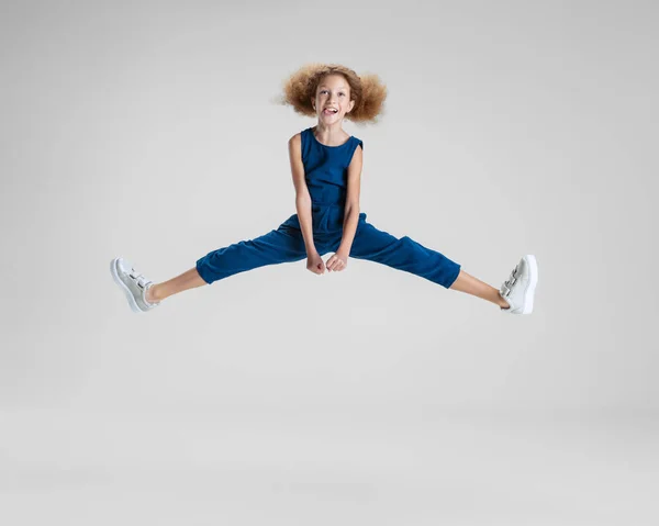 Salah satu gadis lucu Kaukasia kecil dengan baju biru melompat tinggi dan bersenang-senang terisolasi di atas latar belakang studio putih. — Stok Foto