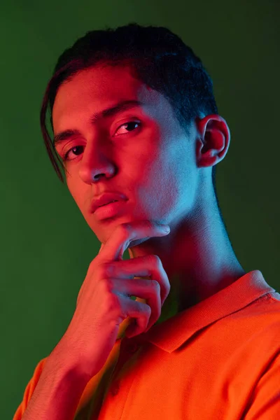 Close-up portret van jonge man, student poseren geïsoleerd op groene studio backgroud in neon licht. Menselijke emoties concept. — Stockfoto