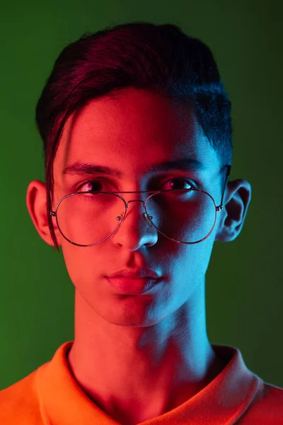 Gros plan portrait de jeune homme, étudiant posant isolé sur fond de studio vert sous la lumière du néon. Concept des émotions humaines. — Photo