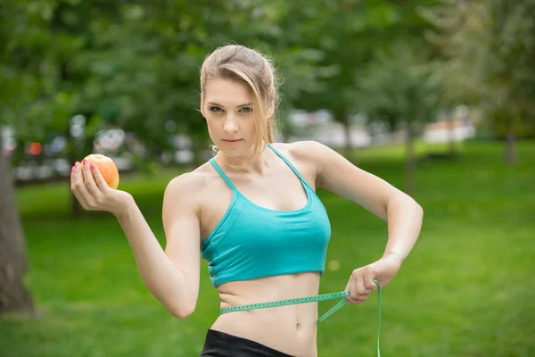 Sportowy młoda kobieta z jabłkiem i miarkę. Na zewnątrz. — Zdjęcie stockowe