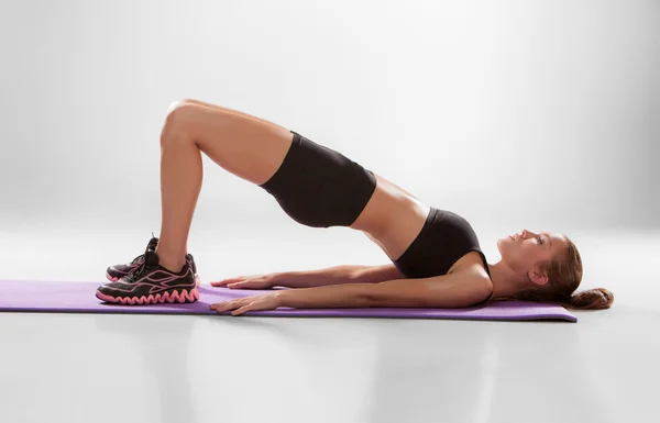 Aantrekkelijke vrouw doen fitness oefening op een Lila mat — Stockfoto