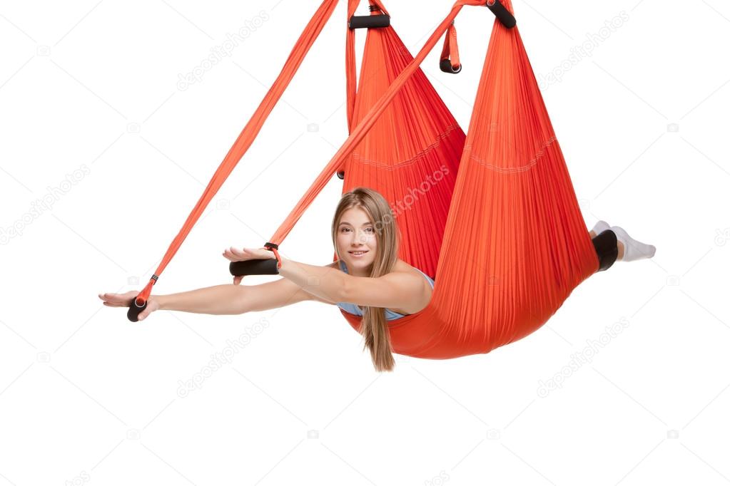 Young woman doing anti-gravity aerial yoga in hammock on a seamless white background.