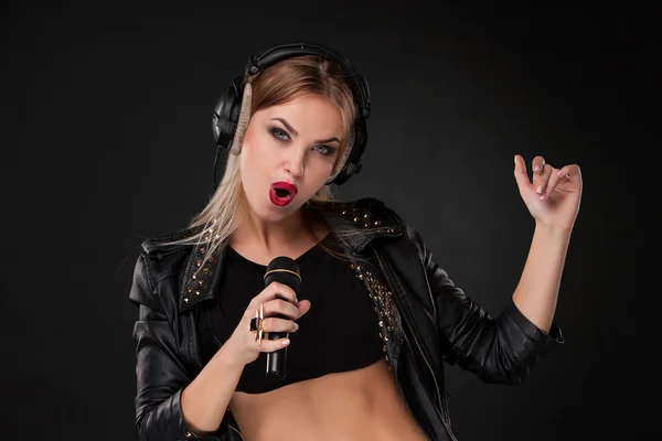 Retrato de una hermosa mujer cantando en el micrófono con auriculares en el estudio sobre fondo negro — Foto de Stock