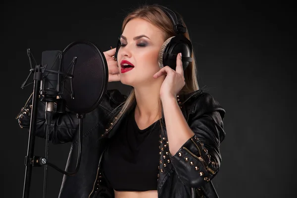 Retrato de una hermosa mujer cantando en el micrófono con auriculares en el estudio sobre fondo negro —  Fotos de Stock