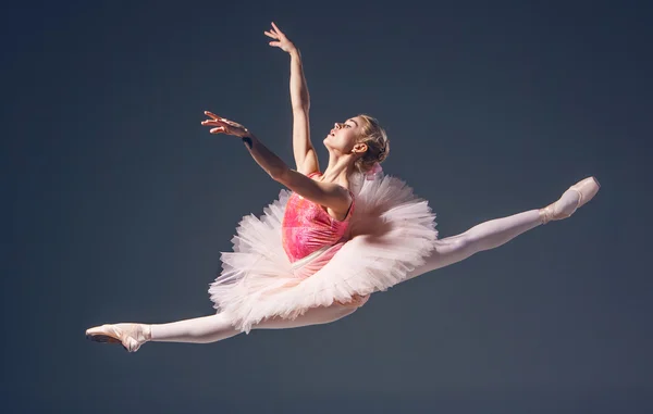 Mooie vrouwelijke balletdanser op een grijze achtergrond. Ballerina is het dragen van roze tutu en pointe schoenen. — Stockfoto