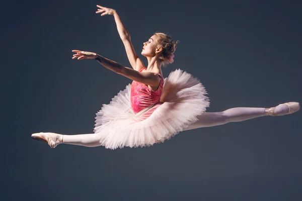 Mooie vrouwelijke balletdanser op een grijze achtergrond. Ballerina is het dragen van roze tutu en pointe schoenen. — Stockfoto