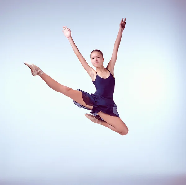 Schöne junge Balletttänzerin springt auf einem grauen Hintergrund. — Stockfoto