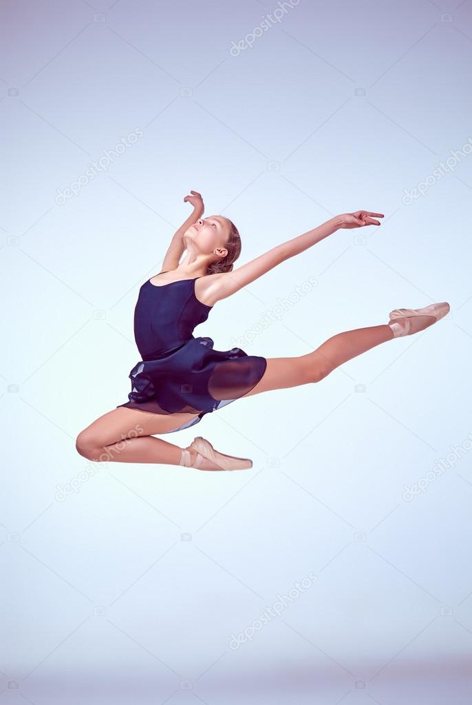 Beautiful young ballet dancer jumping on a gray background. 