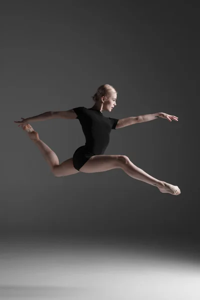 Young beautiful modern style dancer jumping on a studio background — Stock Photo, Image