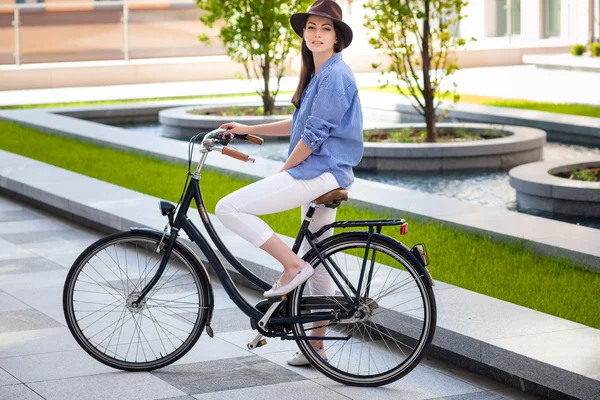 Mooi meisje in hoed een fiets op straat — Stockfoto