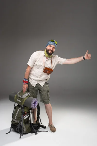 Male tourist with backpack hitchhiking on gray background — Stok fotoğraf