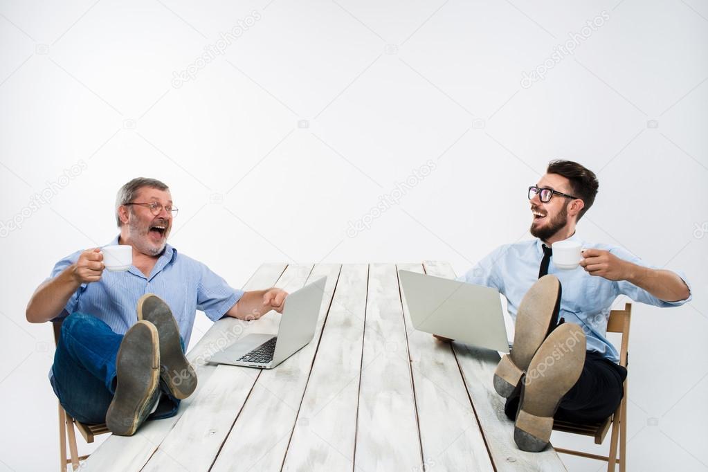 The two businessmen with legs over table working on laptops