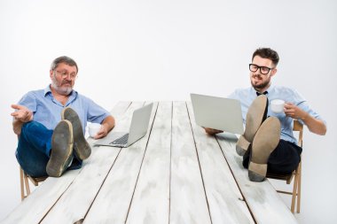 The two businessmen with legs over table working on laptops clipart