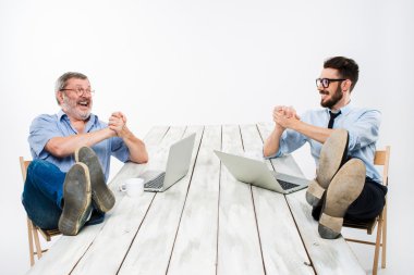 The two businessmen with legs over table working on laptops