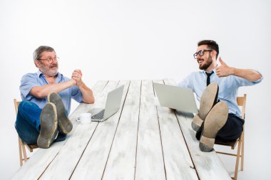 The two businessmen with legs over table working on laptops