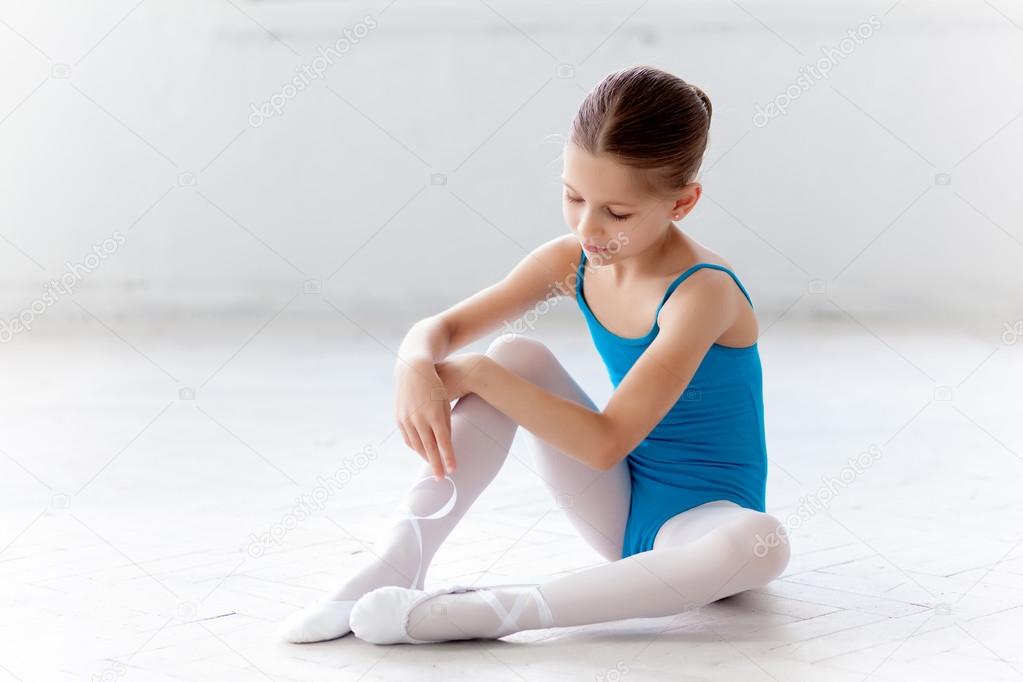 Beautiful little ballerina in blue dress for dancing puting on foot pointe shoes