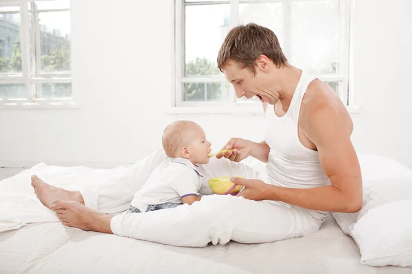 Молодий батько з дев'ятимісячним сином на ліжку вдома — стокове фото