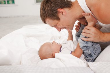 young father with his nine months old son on the bed at home clipart