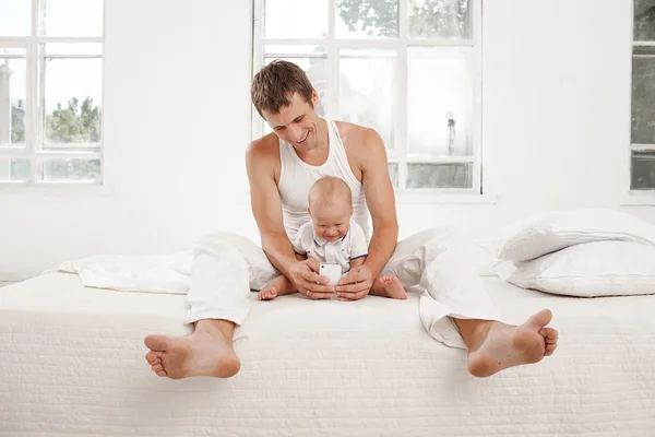 Unga far med sin nio månader gamla son på sängen hemma — Stockfoto