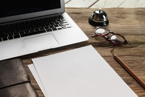 The laptop, blank paper, glasses and small bell on the wooden table — Stock Photo, Image