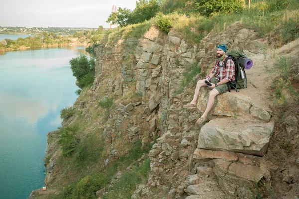 Junge kaukasische Mann mit Rucksack sitzt auf der Spitze des Hügels — Stockfoto