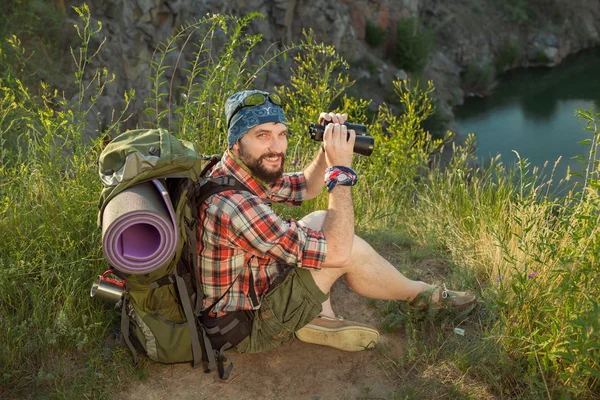 Young caucasian man with backpack sitting on the top of hill — Stock Photo, Image