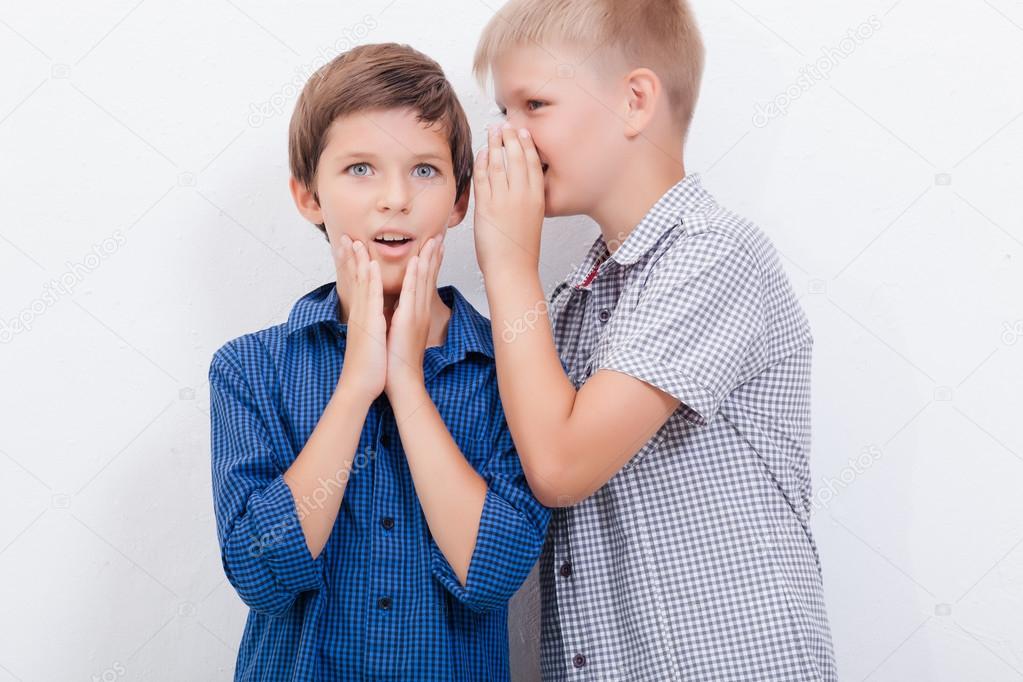 Teenage boy whispering in the ear a secret to friendl on white  background