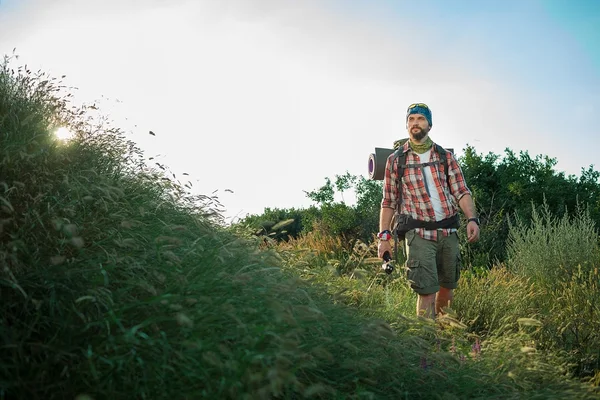 Jeune homme caucasien avec sac à dos marchant sur une prairie verte — Photo