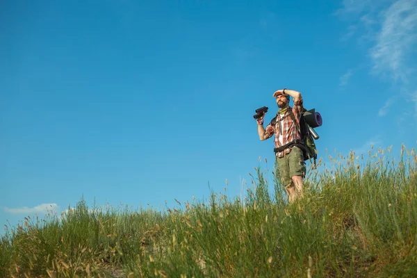 Junger kaukasischer Mann mit Rucksack steht auf dem Gipfel des Hügels — Stockfoto
