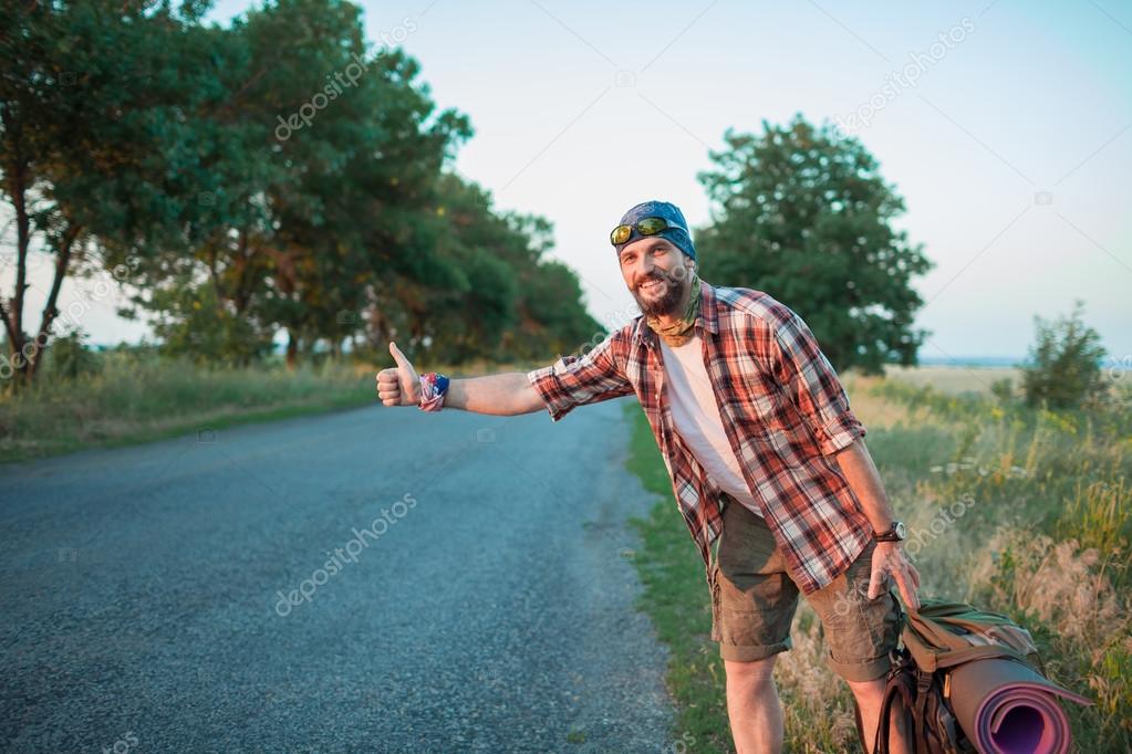 Young smilimg caucasian tourist hitchhiking along a road.
