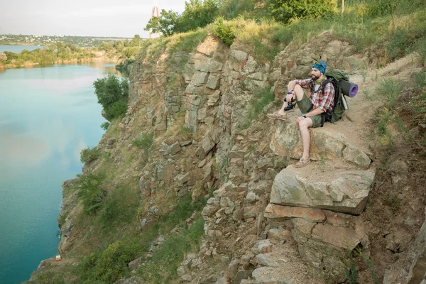 Junge kaukasische Mann mit Rucksack sitzt auf der Spitze des Hügels — Stockfoto